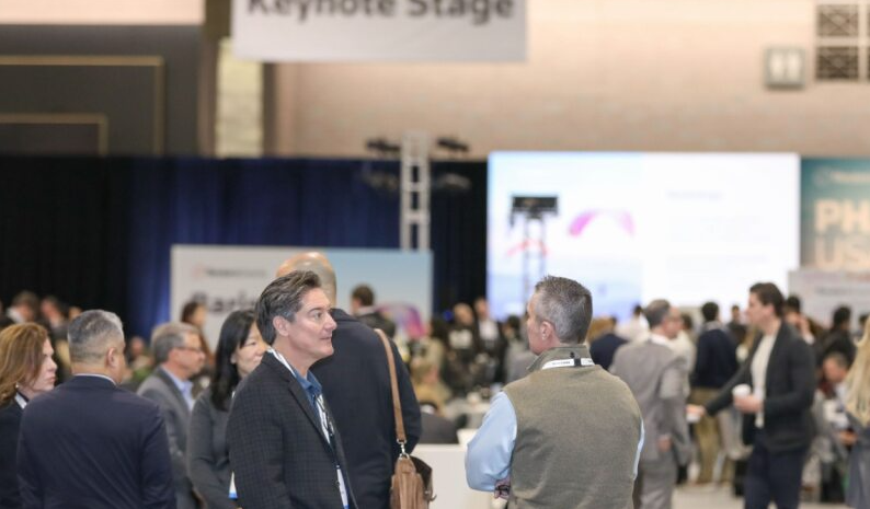 Attendees network in a busy expo hall beneath a "Keynote Stage" sign, with blurred PHARMA USA stage graphics in the background.