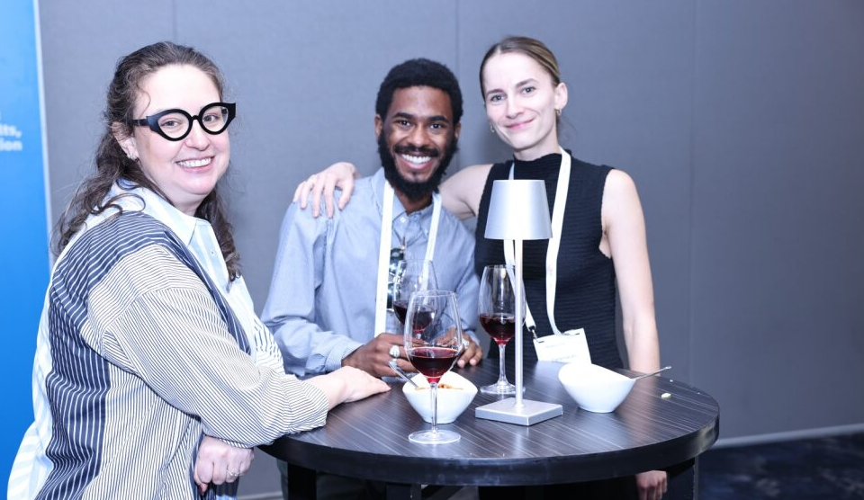 Three happy conference attendees, two women and a man, networking with drinks at a high-top table.