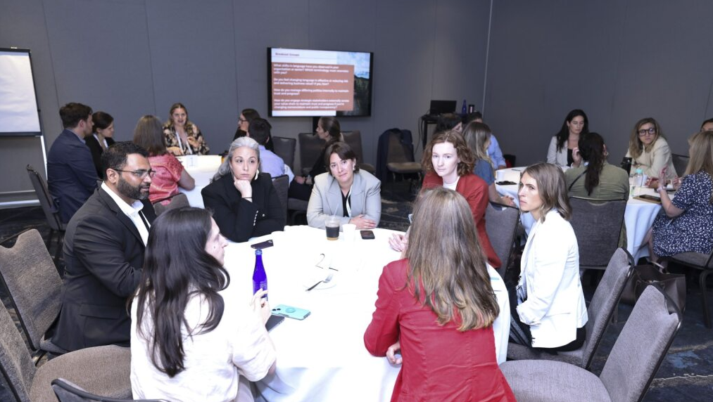 Diverse group of attendees participating in a breakout session at a round table, with discussion prompts on a screen.
