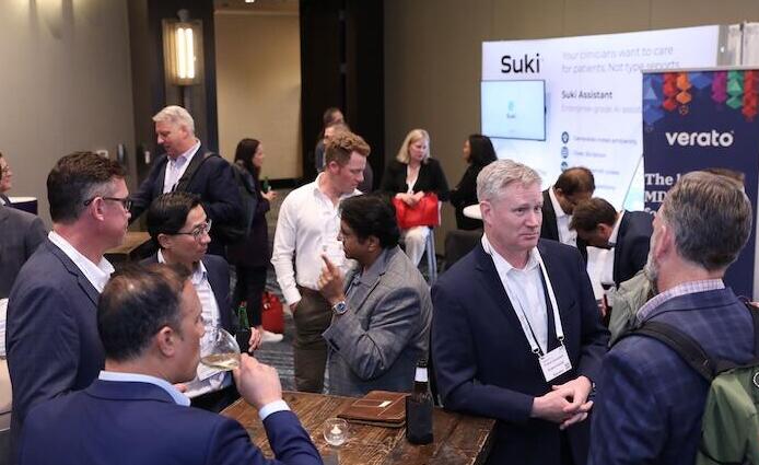A bustling area of the conference floor, with attendees networking near "Suki" and "Verato" brand displays.
