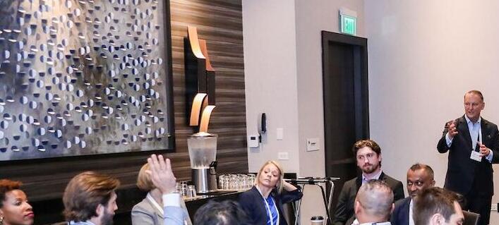 Attendees during a roundtable session with a presenter gesturing at the front, one person has their hand raised