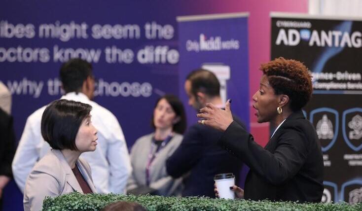 A group of attendees in discussion near a large "ADvantage" banner, with one woman speaking animatedly.