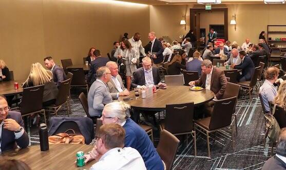 A wide shot of a busy conference hall with many attendees seated at round tables and networking.
