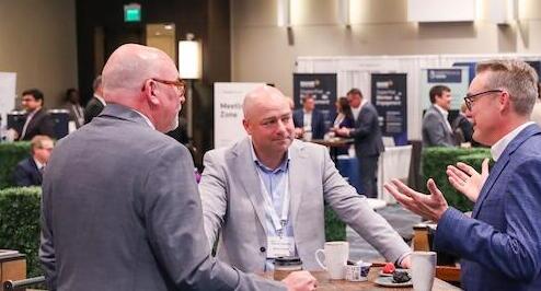 Three men in suits having an animated conversation, one gesturing, at a digital health conference.