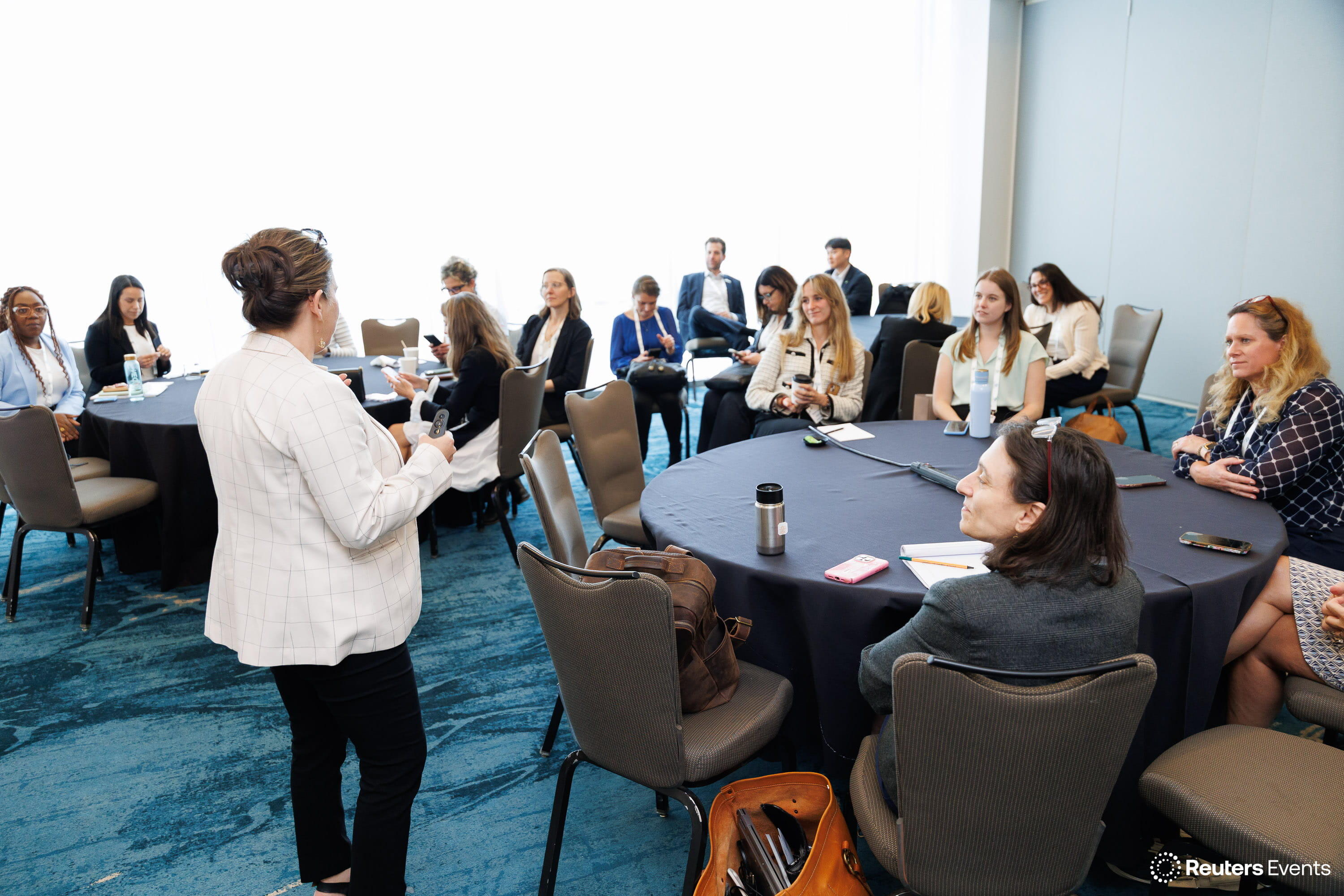 Speaker addressing a room of seated attendees at round tables in a breakout session