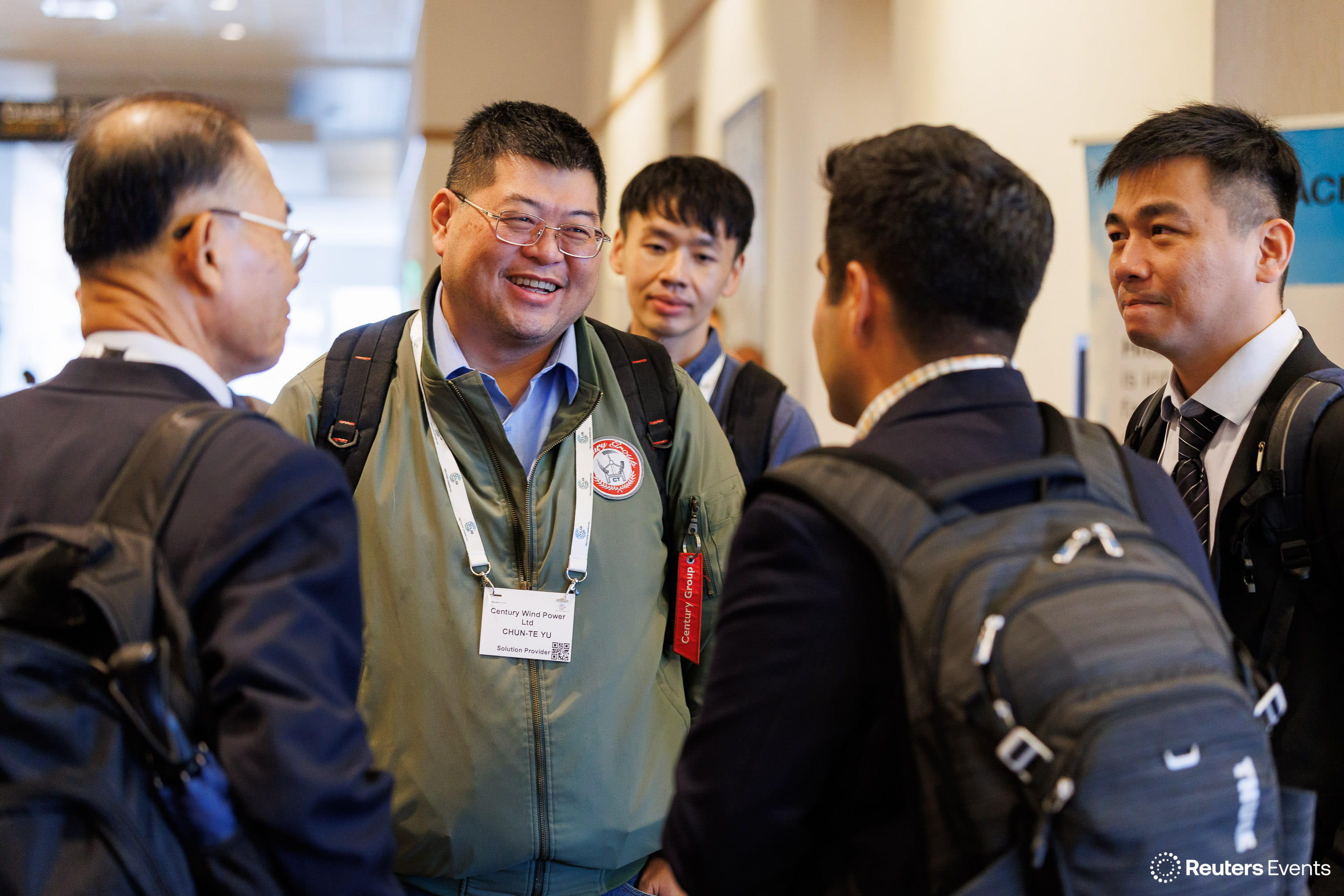 Group of five attendees networking in a conference hallway, one wearing a Century Wind Power badge