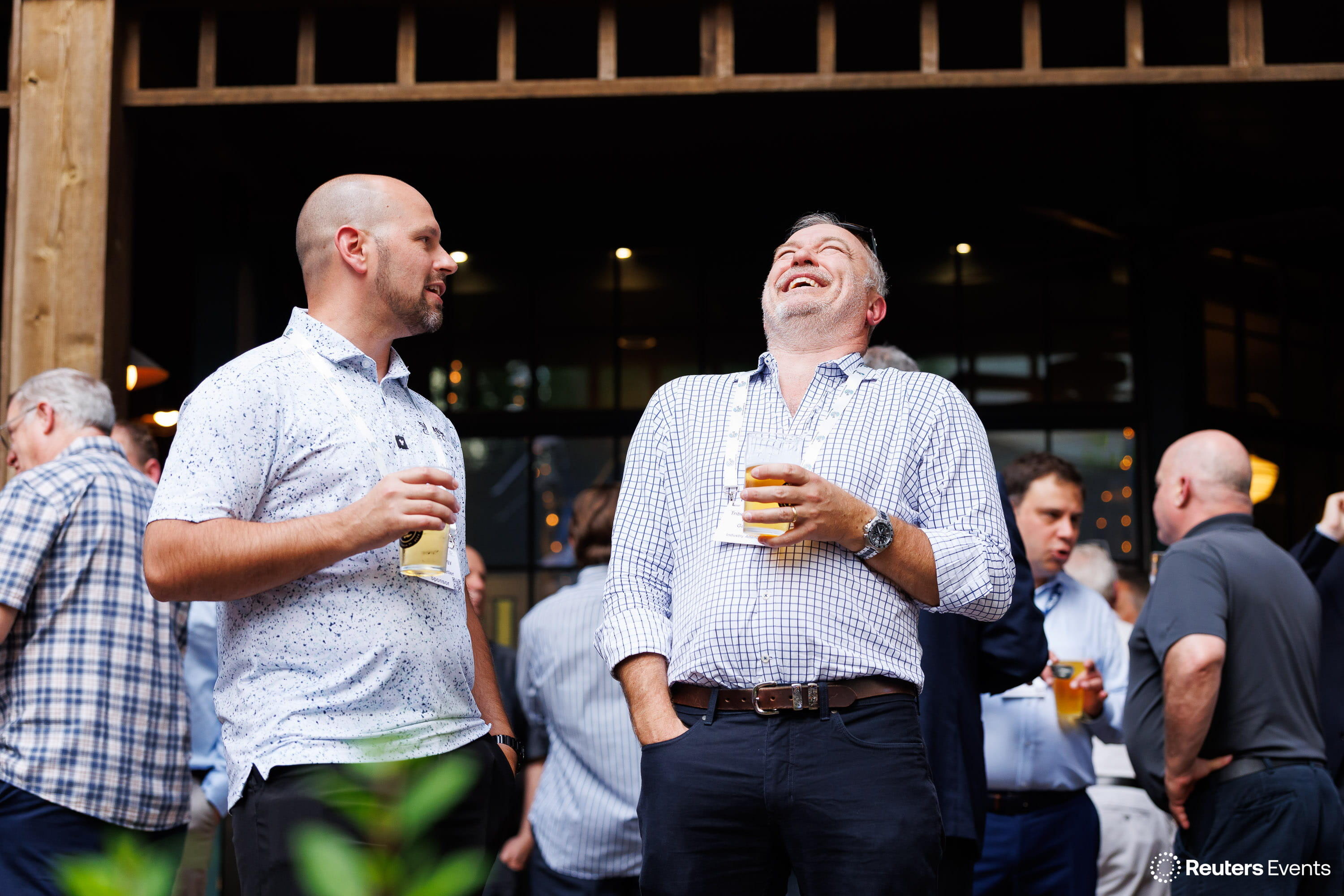Two men laughing together with drinks at an outdoor networking reception