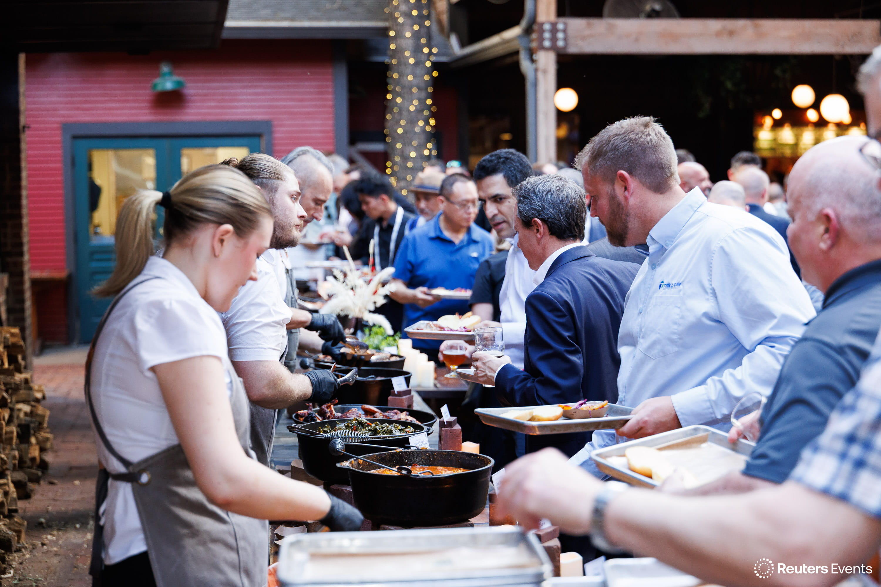 Chefs serving conference attendees along an outdoor buffet at an evening reception
