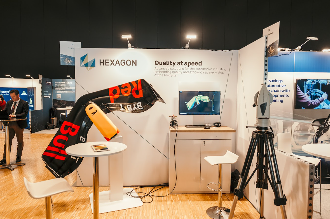 The Hexagon booth at Automotive Europe, featuring an inflatable Red Bull racing wing, a monitor displaying automotive design, and a Leica Absolute Tracker.