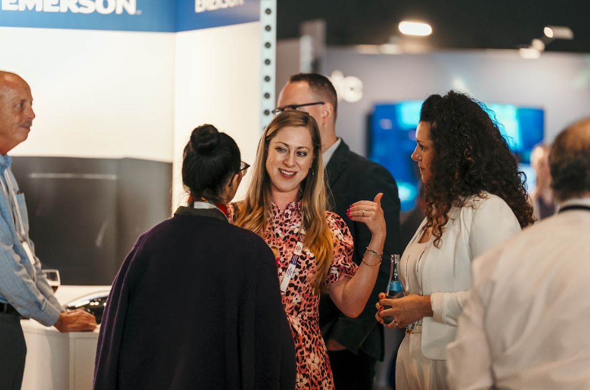 Attendees conversing and networking at a conference, with a woman in a leopard print dress speaking animatedly.