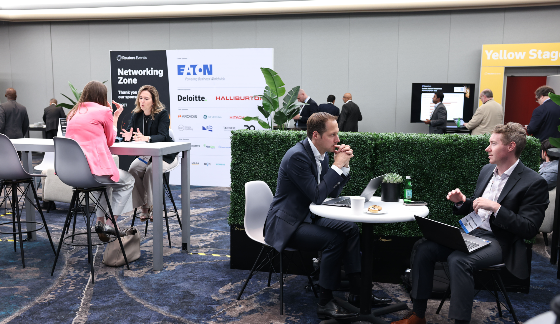 Attendees networking at a Reuters Events conference, with several people engaged in conversations at high-top tables and a "Networking Zone" sign visible in the background.