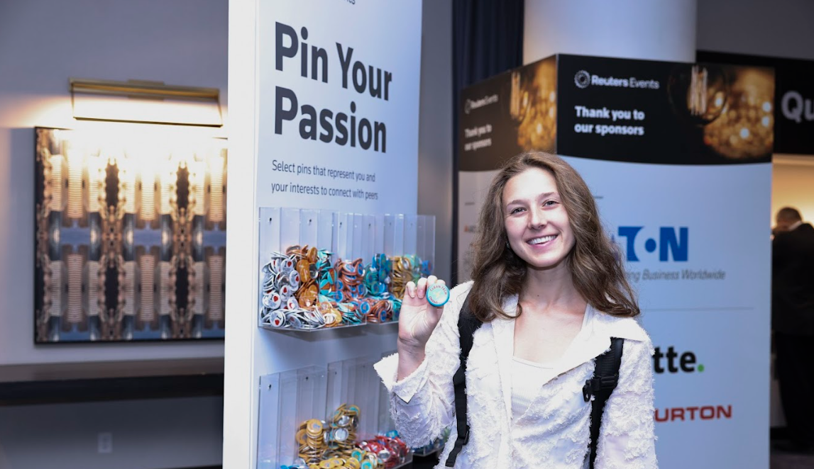 Conference attendee smiling and holding up a pin in front of a "Pin Your Passion" display wall.