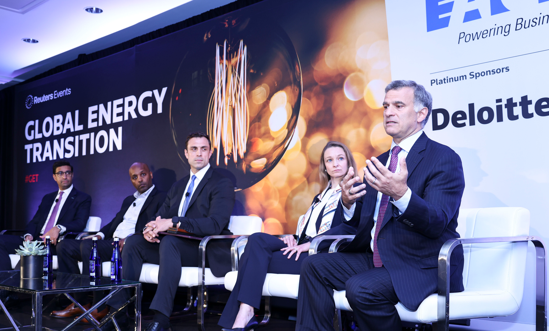 Panelists at the Reuters Events Global Energy Transition conference, with a large lightbulb graphic in the background