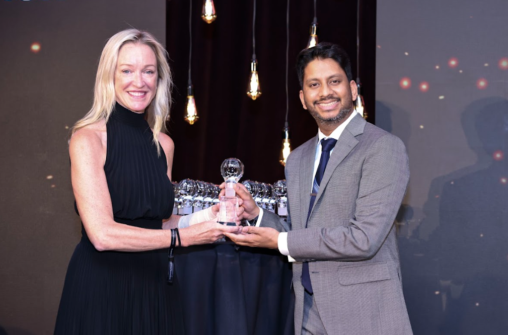 Two conference delegates smiling while presenting an award trophy on stage.