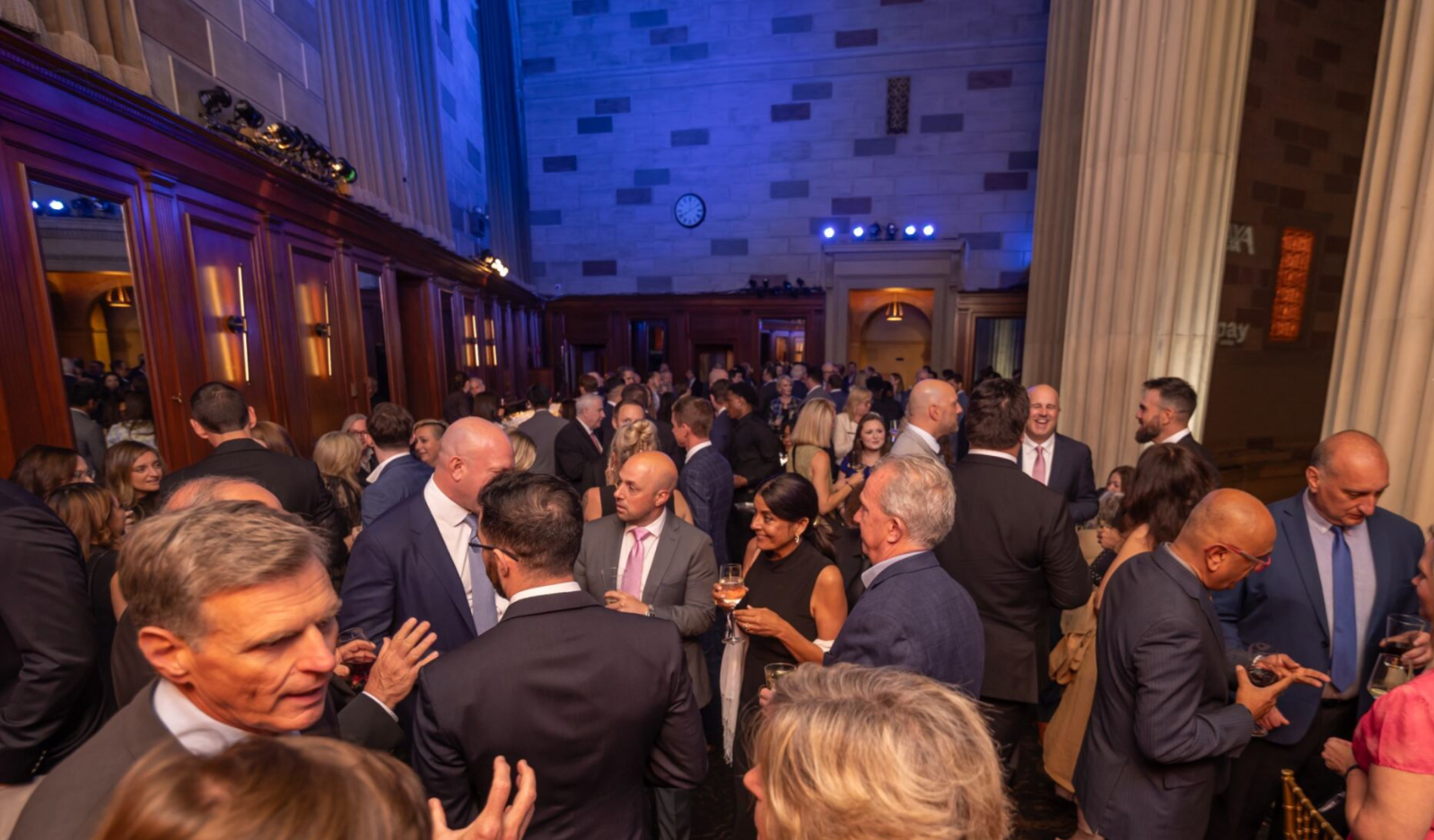 Crowded networking reception in a grand hall with attendees in formal attire.