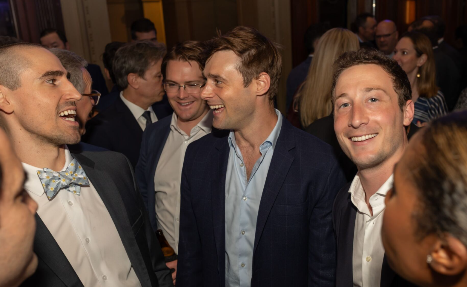 Event attendees in suits talking and smiling at a reception.