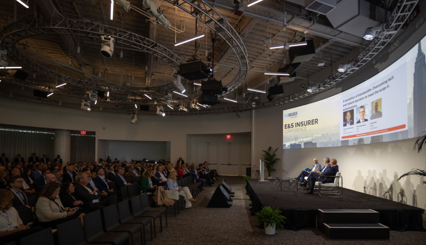 Audience watching a panel discussion on stage at the E&S Insurer Conference.