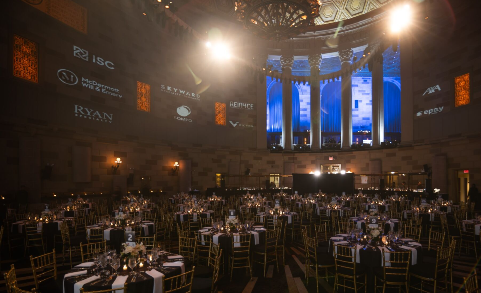 Ballroom set for a formal gala dinner with round tables and stage.