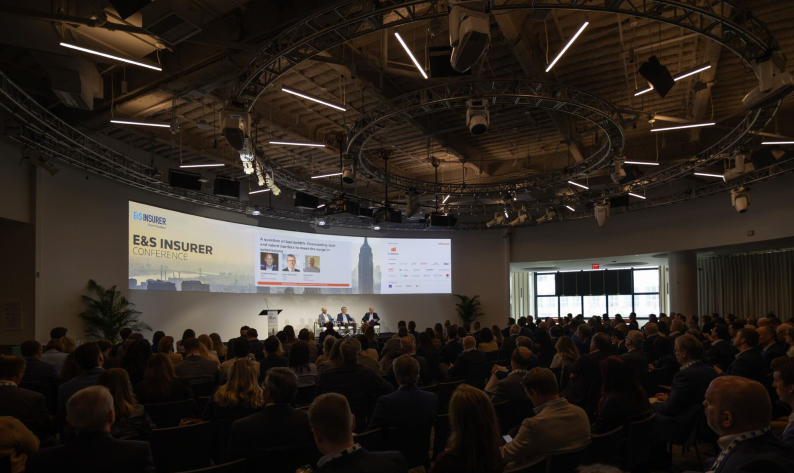 Audience watching a panel discussion on stage at the E&S Insurer Conference.