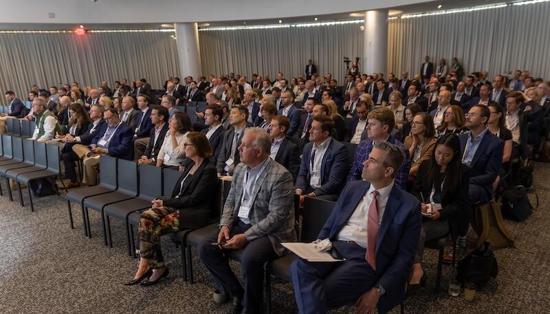 Large seated audience in a conference room watching a presentation.