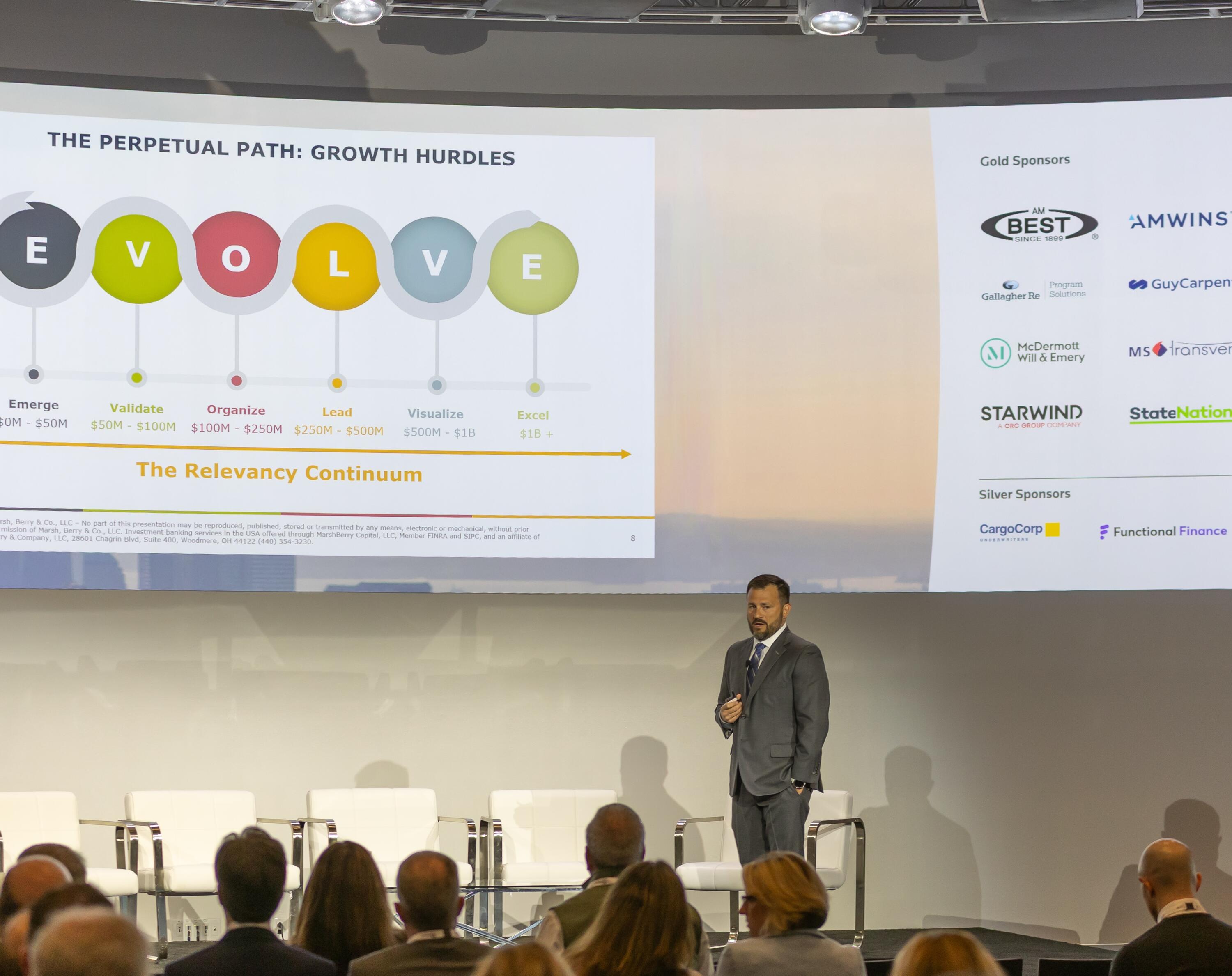 Speaker on stage presenting a slide titled "Evolve" at a business conference.