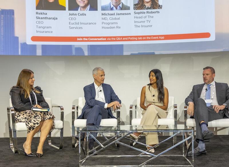 Panel of four speakers seated on white chairs having a discussion on stage.