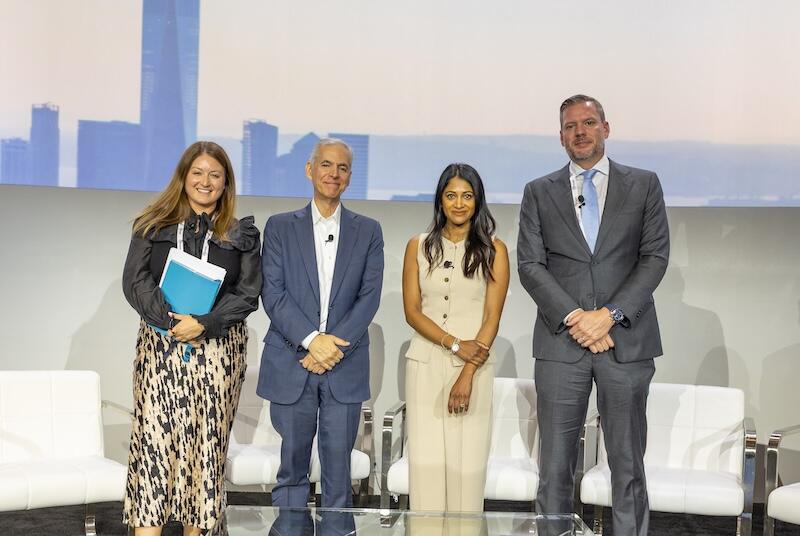 Three panelists standing and posing for a photo on stage against a city skyline backdrop.