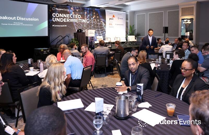 People in a room at tables networking and discussing topics at  Connected Underwriting USA