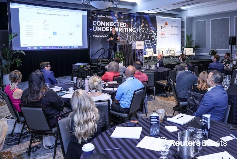 A group of people at tables watching a presenation at a  Connected Underwriting USA event
