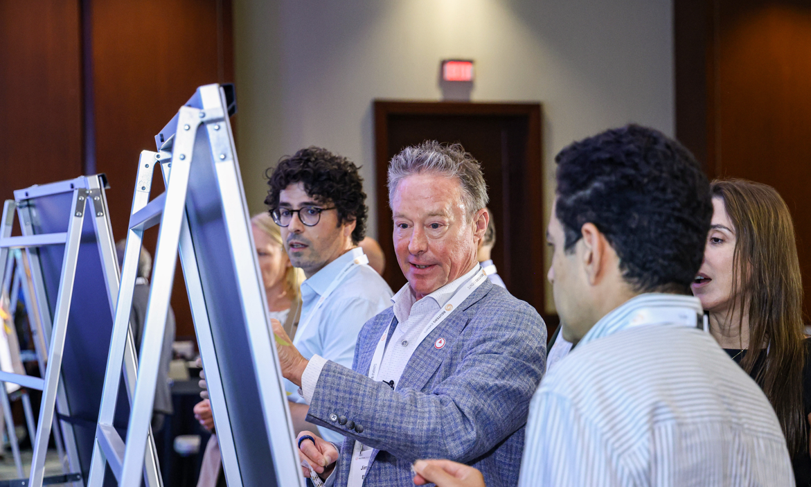 A group of attendees interacts around display boards at a conference.