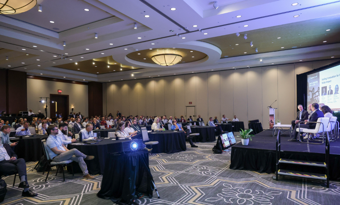 Audience listening to a panel discussion on stage at a large business conference.