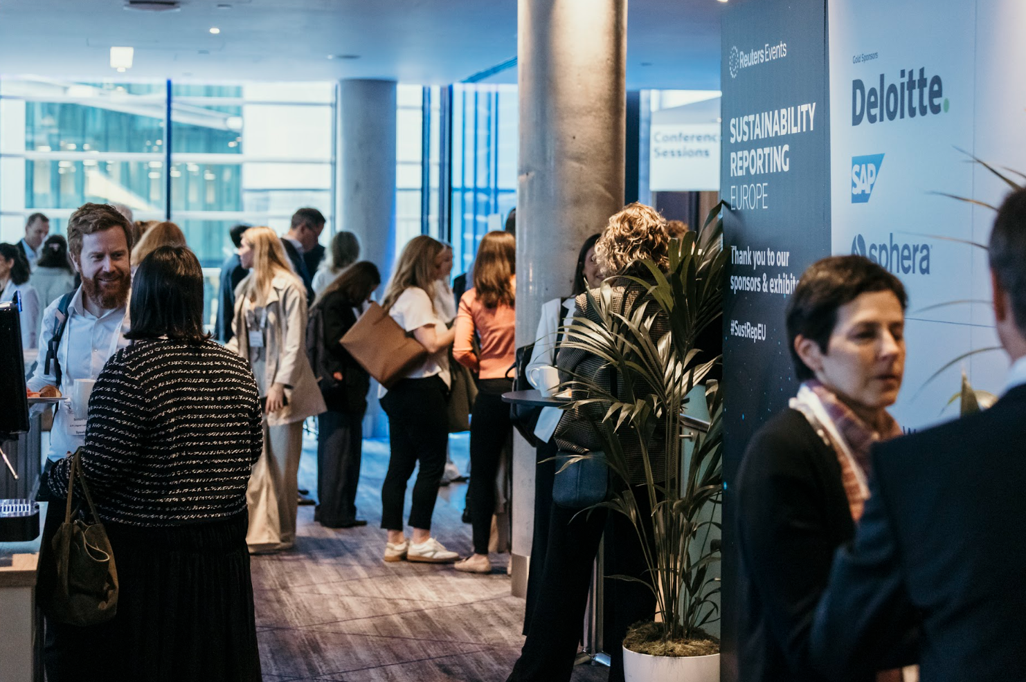 Attendees networking in hallway beside sustainability conference sponsor wall