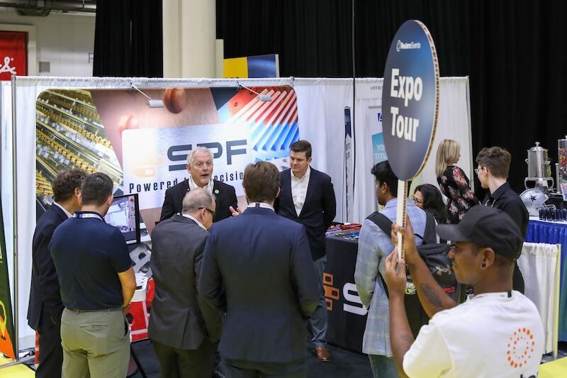 Busy expo hall with attendees networking and chatting around sponsor booths during an interactive break.