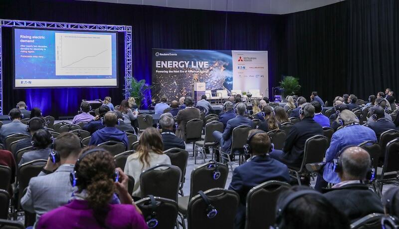 A room ful of people sitting wathcing a presentation with a speaker on stage