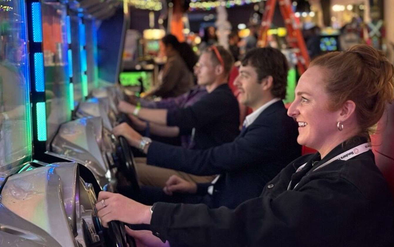 People playing arcade racing games in a row.