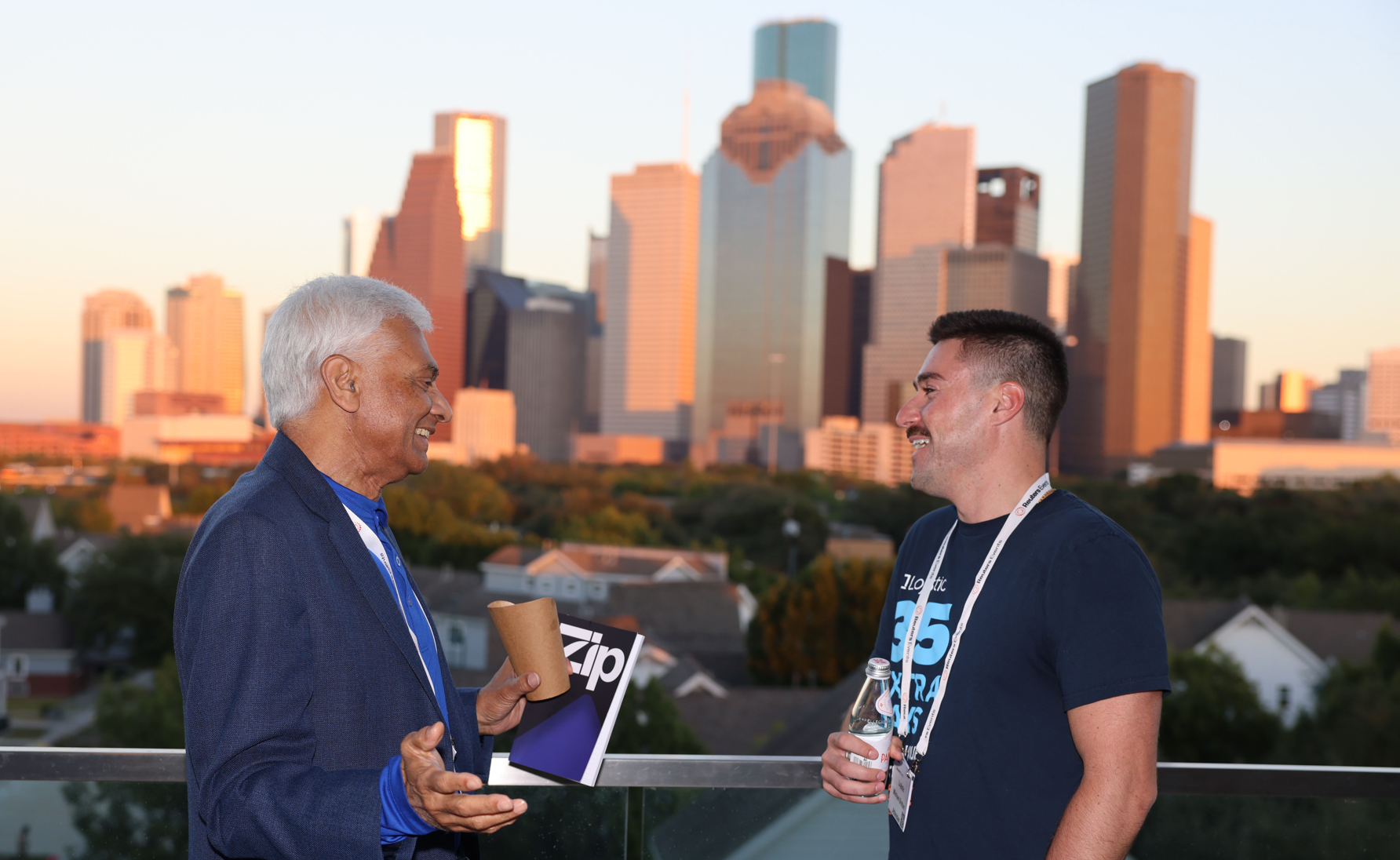 Two people talking on a terrace with a city skyline in the background.