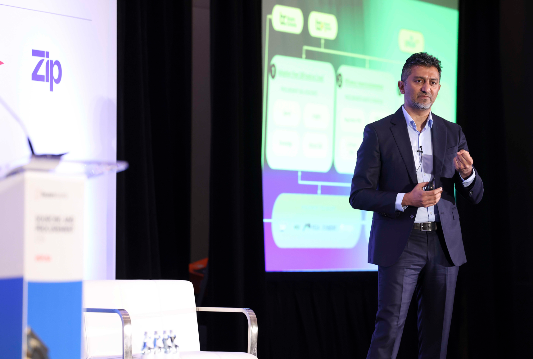Speaker presenting on stage in front of a slide.