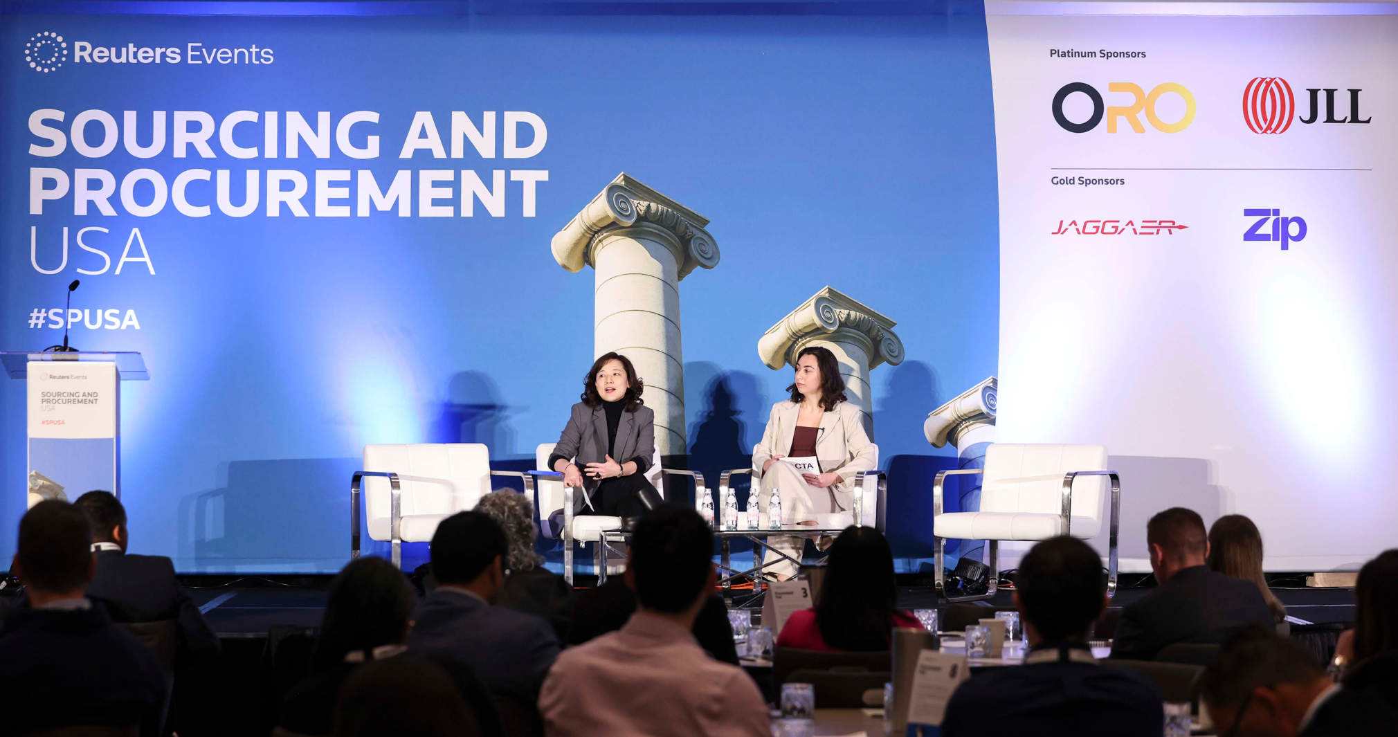 Two speakers seated on stage at Reuters Events "Sourcing and Procurement USA," with audience in the foreground.
