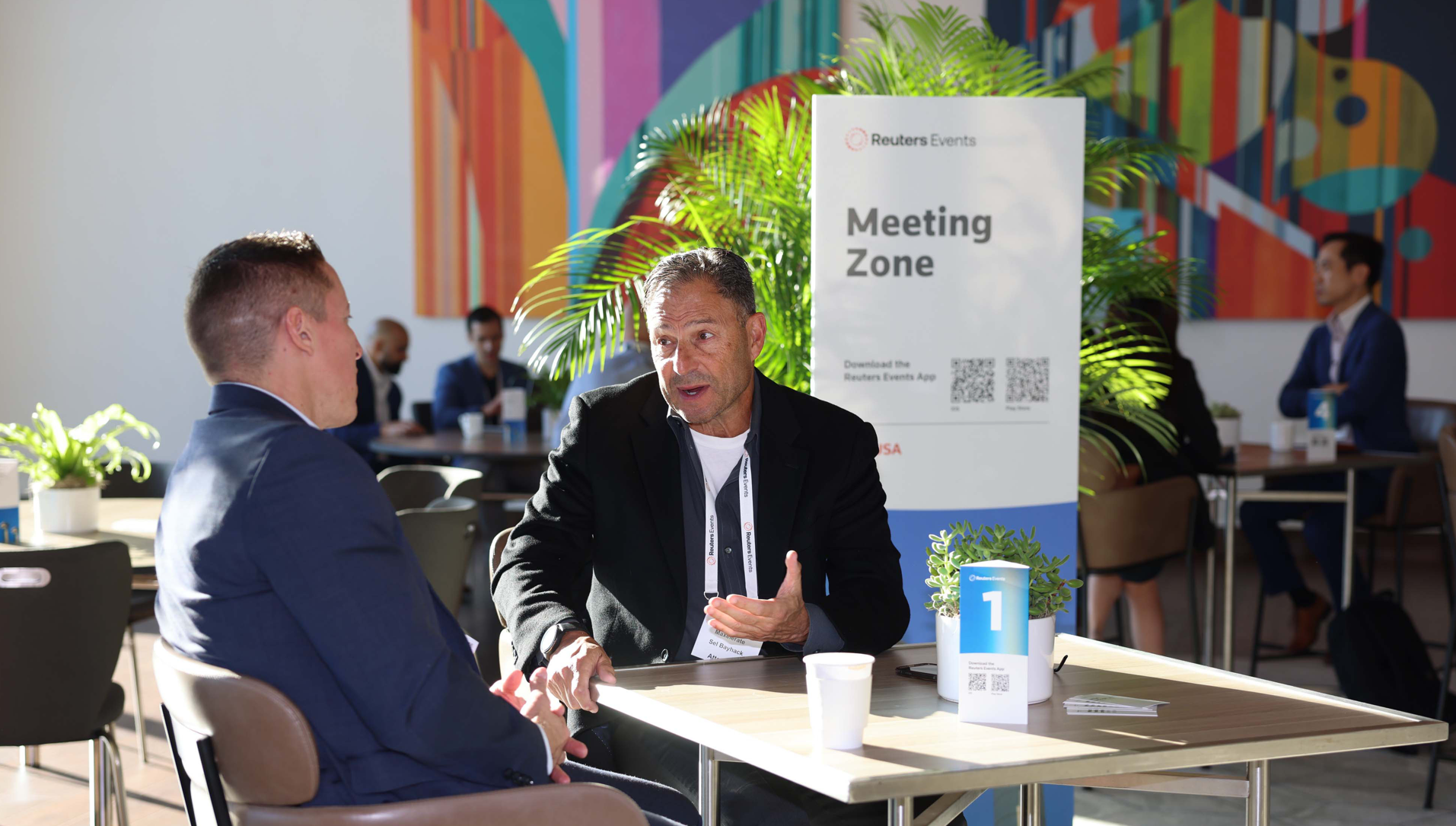 Two people talking at a table in a "Meeting Zone" area.