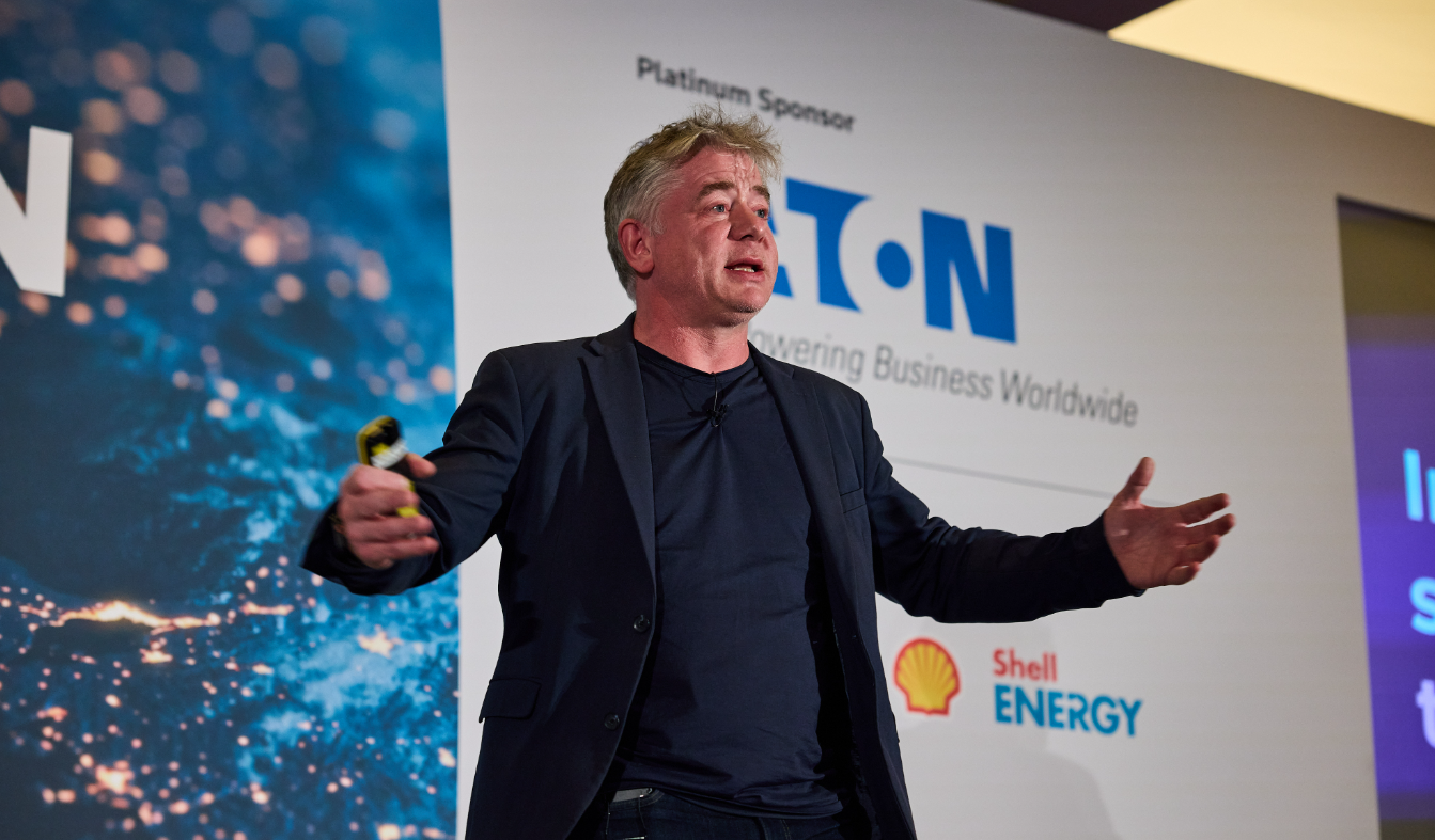 Speaker presenting on stage in front of Eaton and Shell Energy sponsor backdrop.