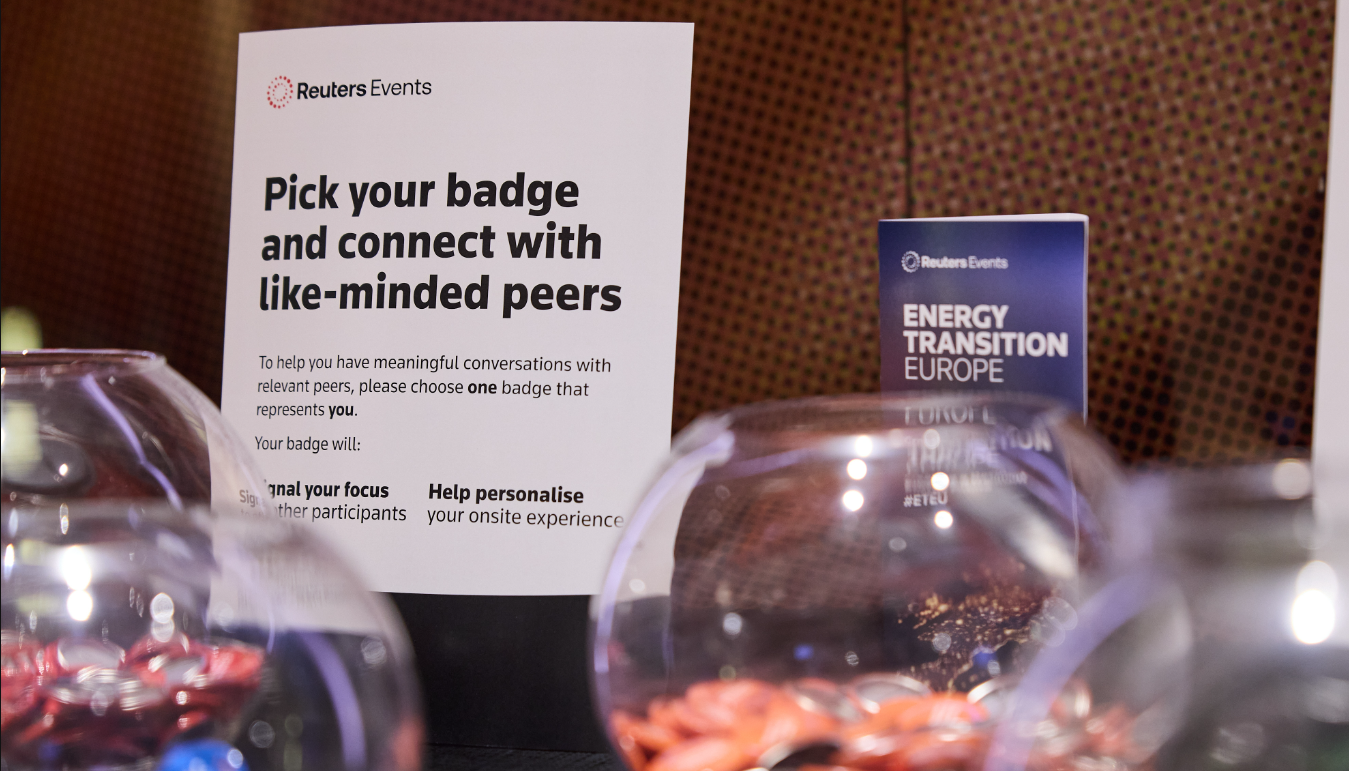 Reuters Events sign reading "Pick your badge and connect with like-minded peers," with "Energy Transition Europe" sign in background.