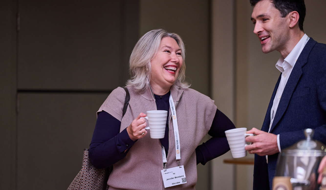 Two conference attendees laughing and chatting while holding coffee mugs.