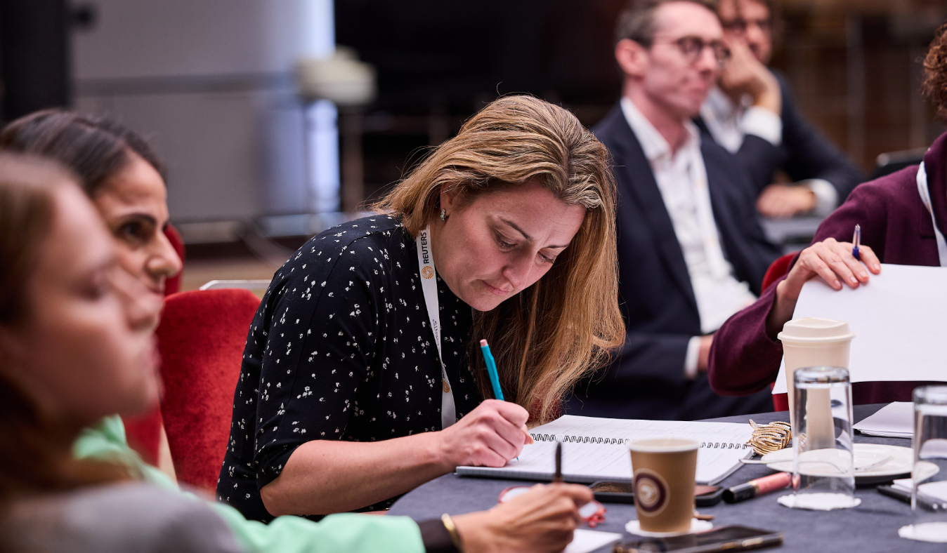 Conference attendee taking notes in a notebook at a roundtable session.
