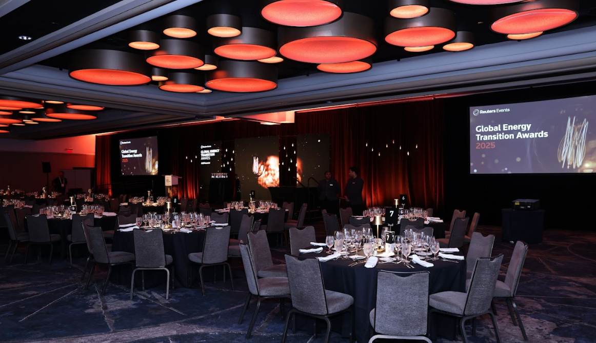 Banquet hall set for the Reuters Events "Global Energy Transition Awards 2025" with round dinner tables and stage screens in the background.