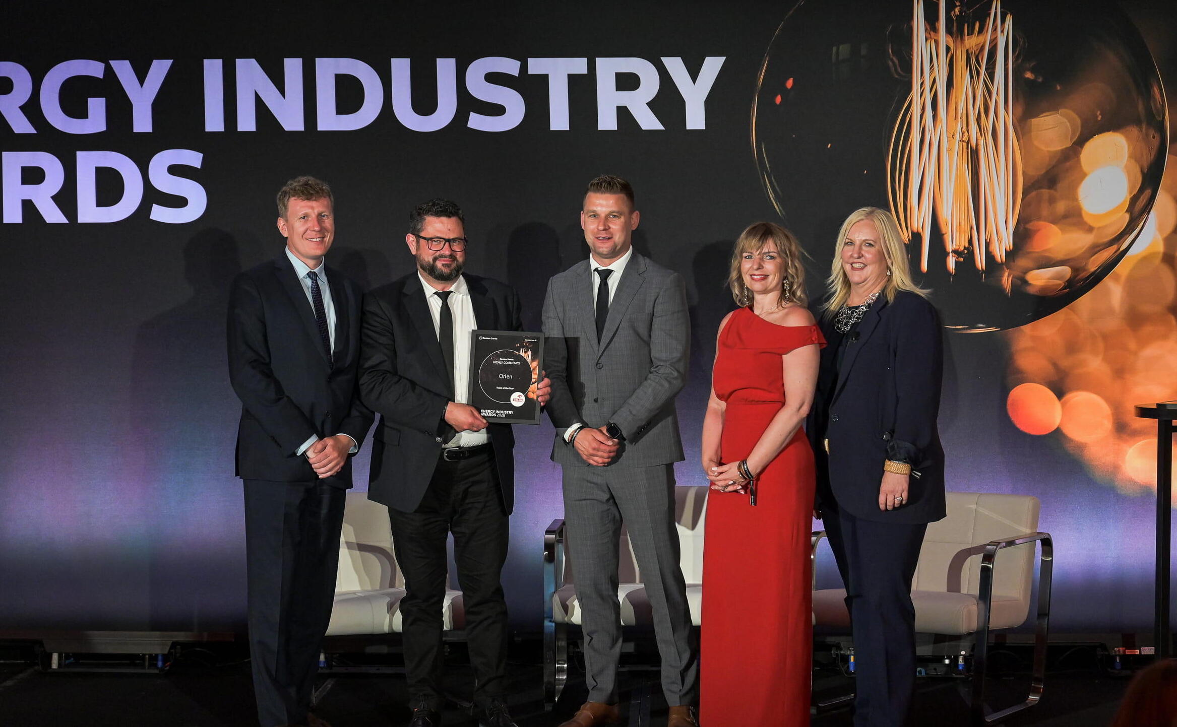 Five award winners and presenters pose on stage holding their Energy Industry Awards trophy, with a large 'Energy Industry Awards' backdrop behind them