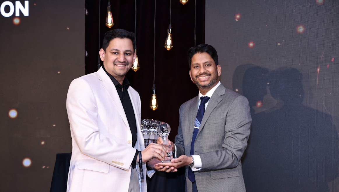Two men in suits smiling and holding an awards trophy together on stage.