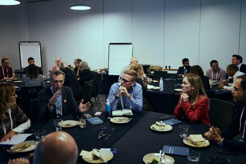 Groups of people sit around roundtables discussing topics.