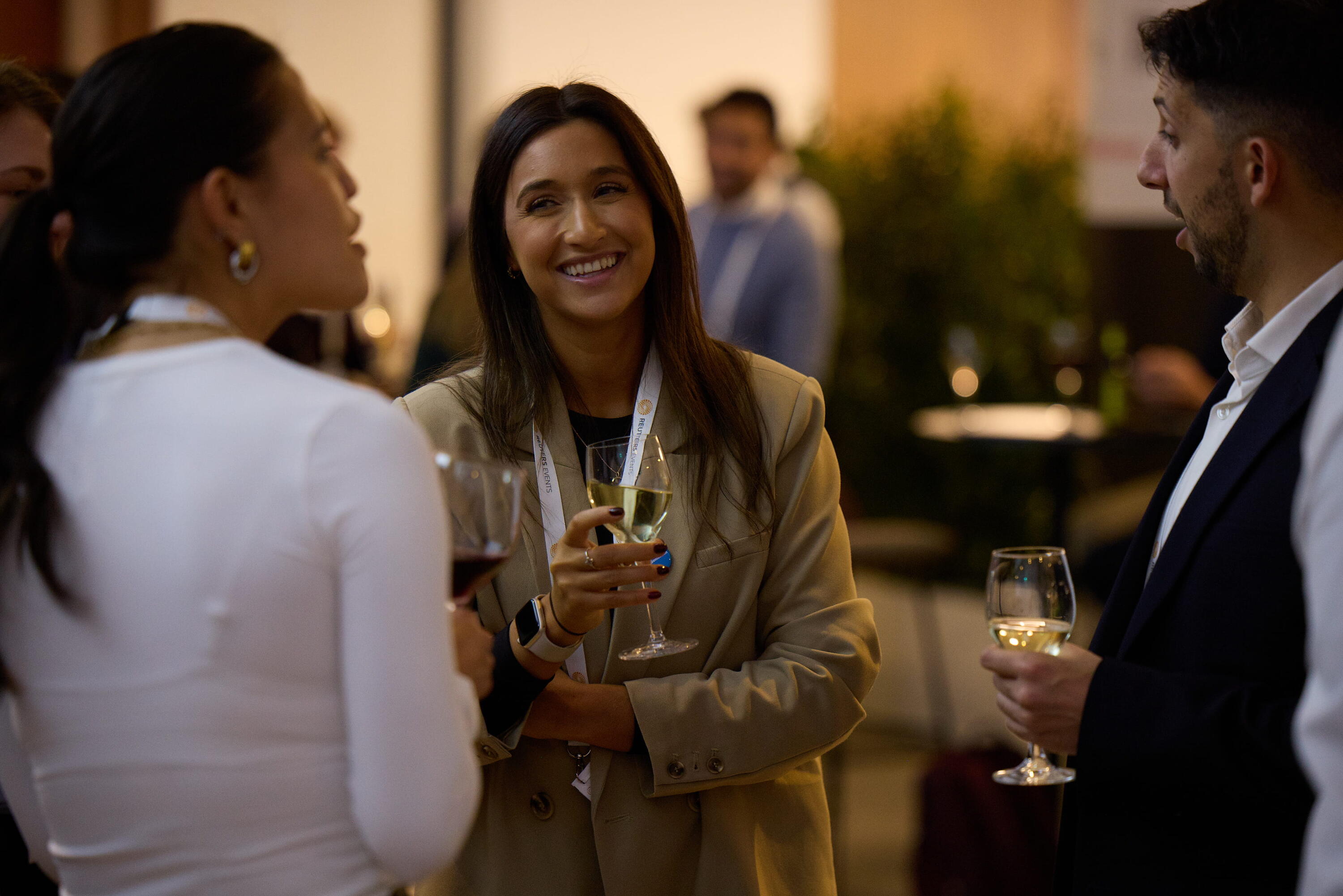 Three conference attendees laugh and socialise over drinks during a networking reception at Reuters Events Sustainability Europe.
