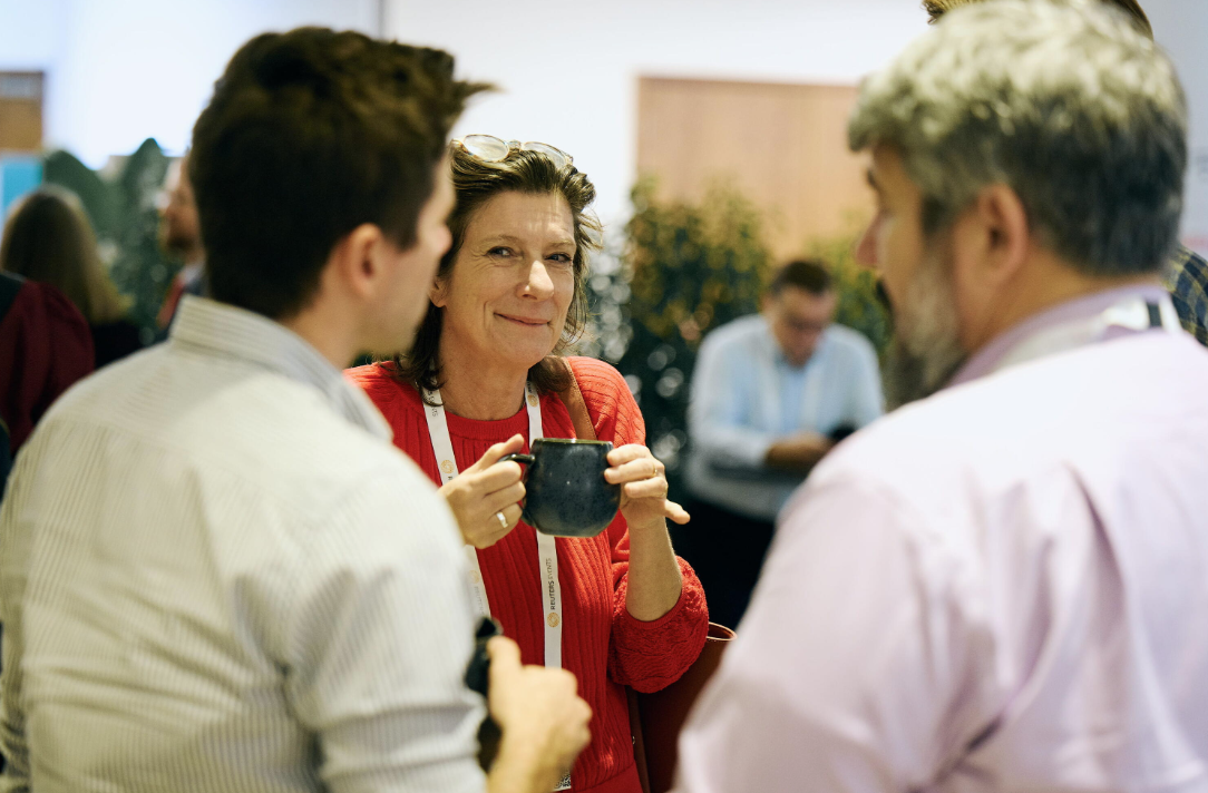 A woman holding a coffee mug smiles while networking with two colleagues at the Reuters Events Sustainability Europe conference.