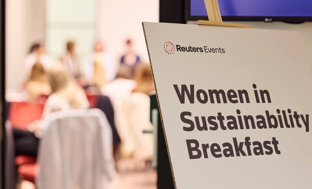 A Reuters Events sign for the "Women in Sustainability Breakfast" in the foreground, with attendees gathered in the background.